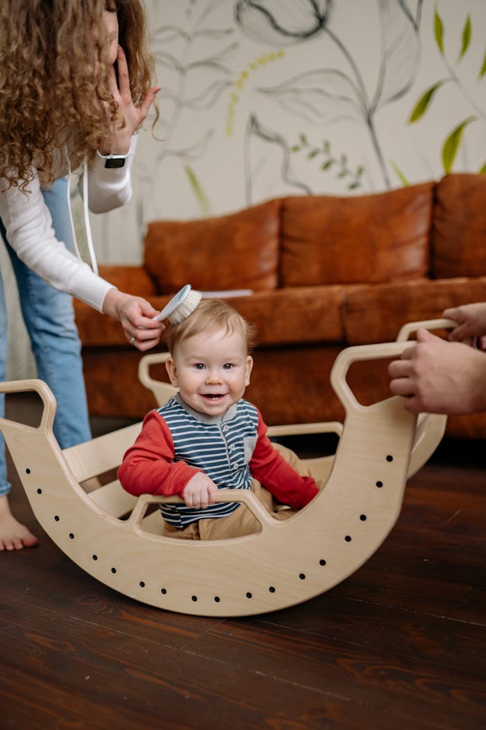 our-story Cute baby smiling in a wooden rocking toy indoors, surrounded by family.